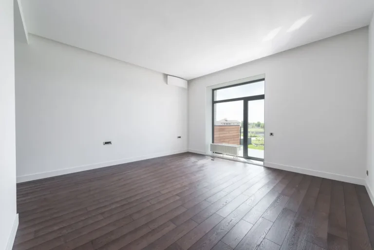 Empty apartment room with wooden flooring and large balcony doors