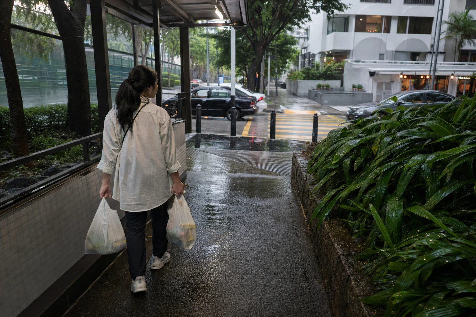 Resident carrying groceries home on a partly covered Central KL pedestrian route during rain