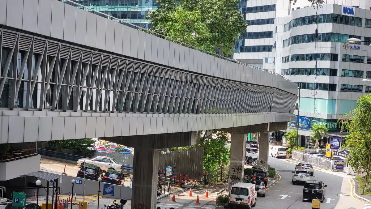 Enclosed KLCC and Bukit Bintang pedestrian bridge passing above a road beside Wisma UOA